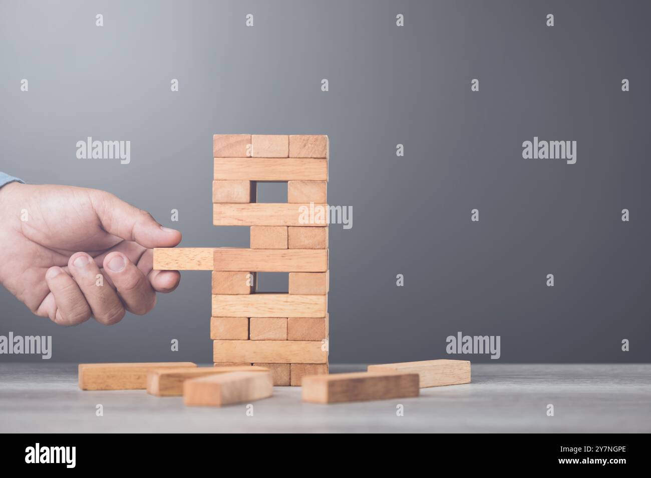 Ein Geschäftsmann denkt über seinen nächsten Schritt in einem Blockspiel auf einem Tisch vor einem grauen Hintergrund nach. Symbolisiert strategisches Denken, Planen Stockfoto