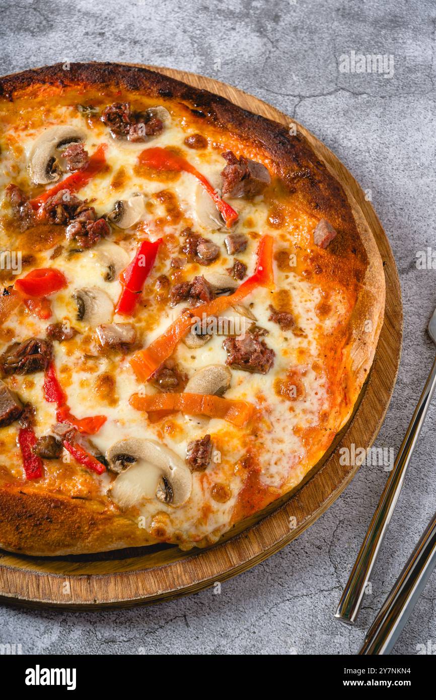 Pizza mit Paprika und Roastbeef auf dem Schneidebrett auf einem Steintisch Stockfoto