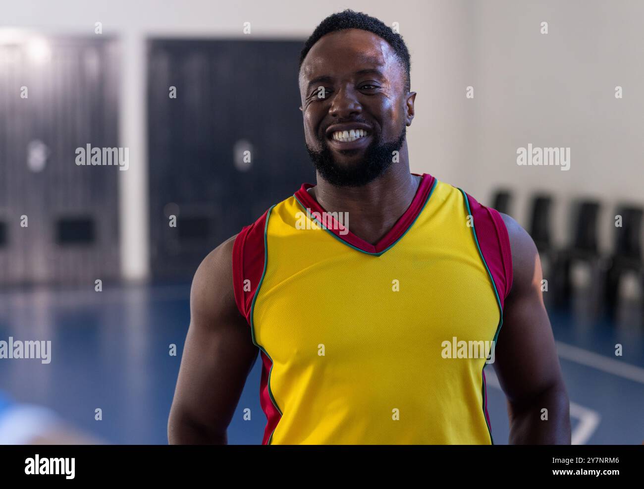 Lächelnder Basketballspieler in gelbem Trikot, der auf dem Hallenplatz steht Stockfoto