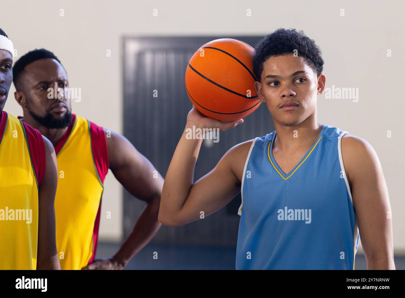 Basketball halten, junger Spieler in blauem Trikot mit Teamkollegen im Fitnessstudio stehen Stockfoto