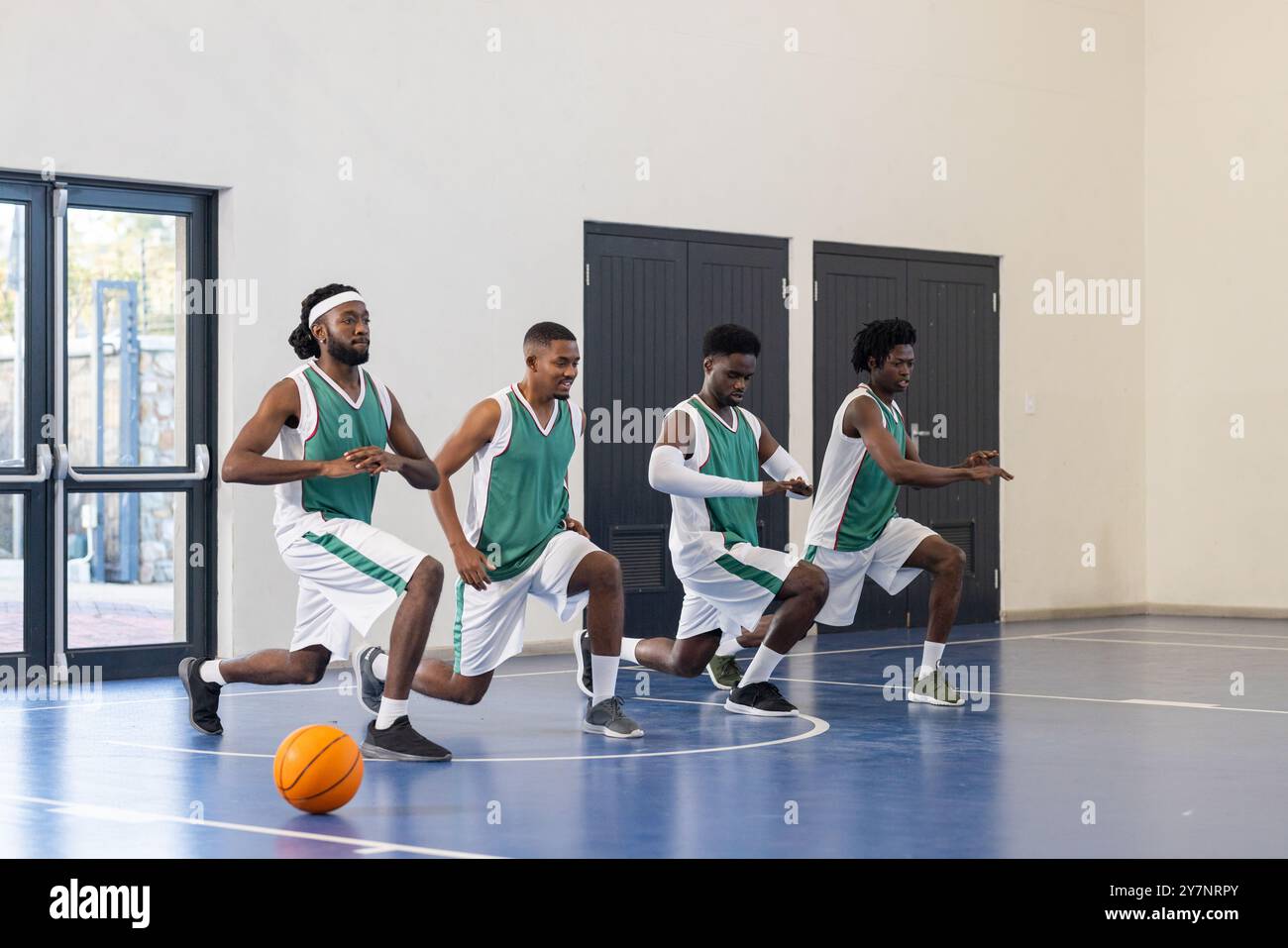 Basketballspieler dehnen sich auf dem Platz aus und bereiten sich auf das Training drinnen vor Stockfoto