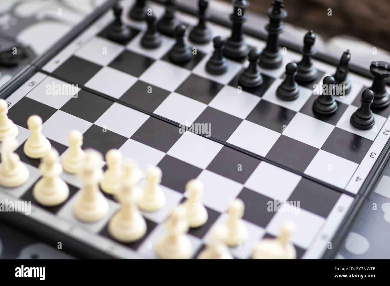 Eine detaillierte Nahaufnahme eines Schachbretts mit weißen und schwarzen Teilen, die strategisch darauf platziert sind, zeigt das komplizierte Design der Spiele Stockfoto