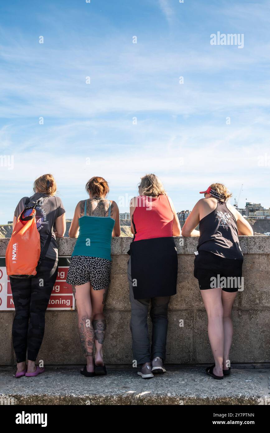 Vier Frauen stehen und blicken über die Hafenmauer im Newquay Harbour Harbor in Newquay in Cornwall in Großbritannien. Stockfoto