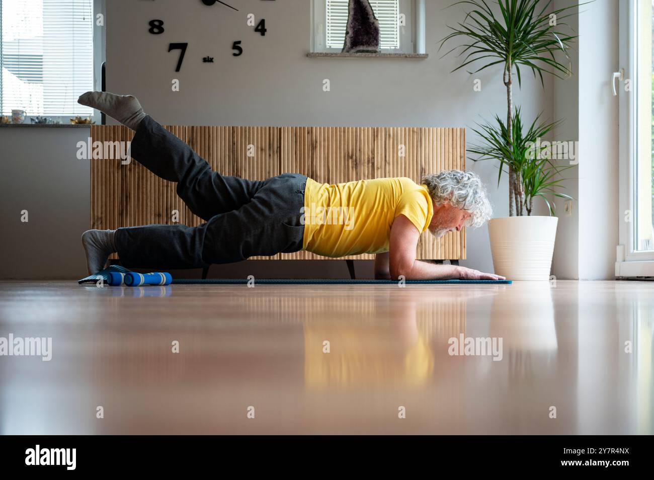 Senior man übt Pilates Plank Übung mit einem angehobenen Bein für einen starken und gesunden Körper und für sein Wohlbefinden und gesunden Ruhestand. Auf einer Yogamatte Stockfoto