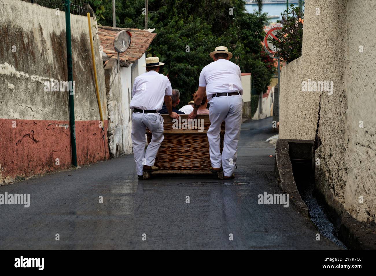 Rodelfahrer in traditionellen weißen Uniformen führen einen Korbschlitten durch die alten Straßen madeiras Stockfoto