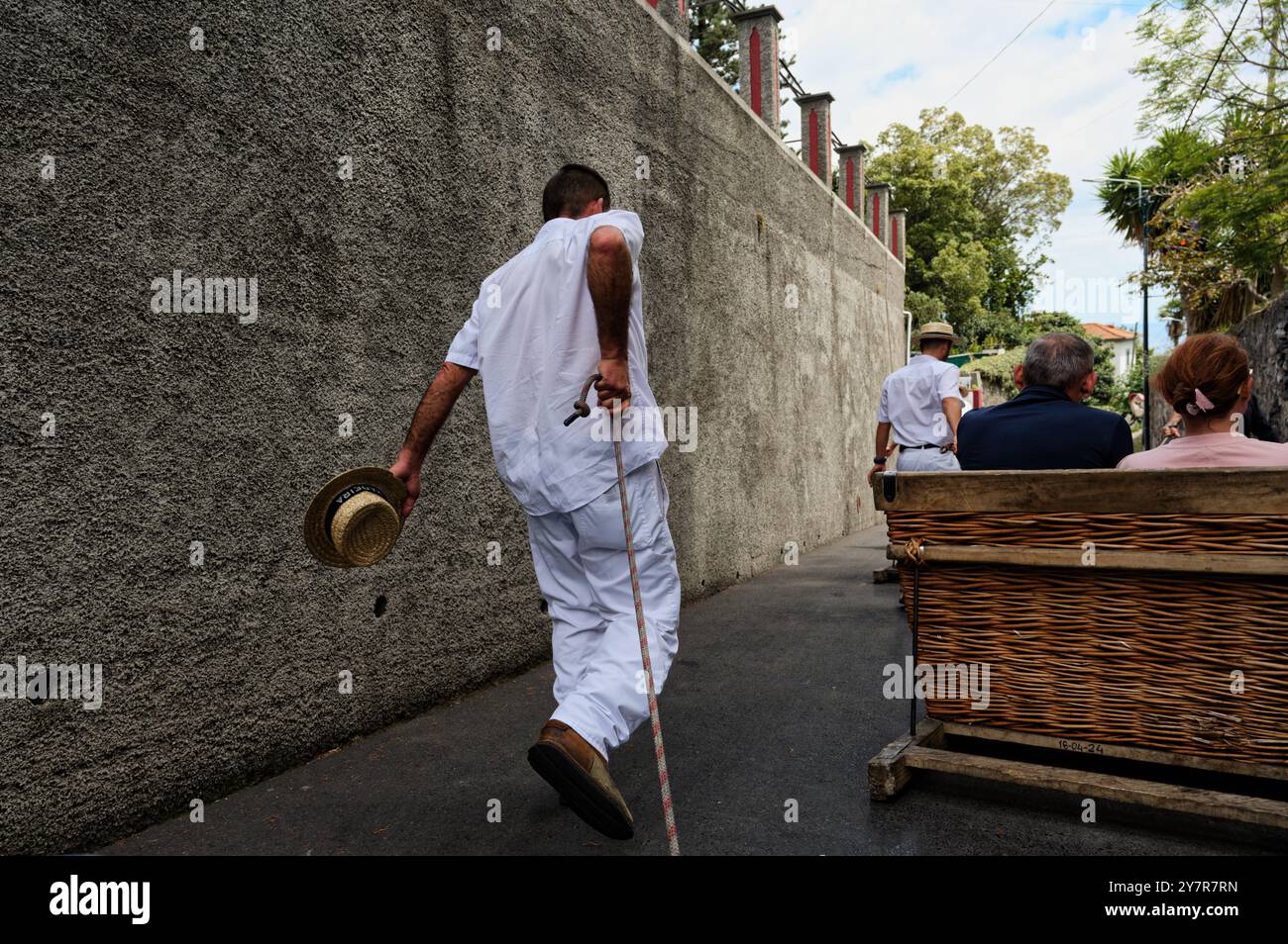Carreiro hält Hut und Seil in der Hand, geht neben einer Korbrodelbahn und nimmt Passagiere durch die Straßen von Funchal Stockfoto