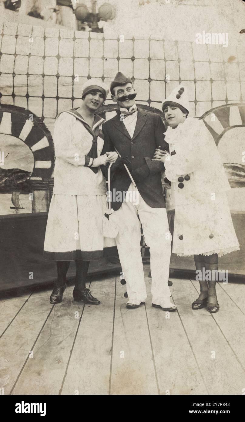 Drei Matrosen, zwei im Schlepptau in pierrette-Kostümen, posieren an Deck. Fotopostkarte, 1910-1919. Matrosen links und rechts im Drag als Pierrettes in Kostümen, die auf Pelissiers Follies basieren. Der Mann in der Mitte trägt einen großen falschen Schnurrbart Stockfoto