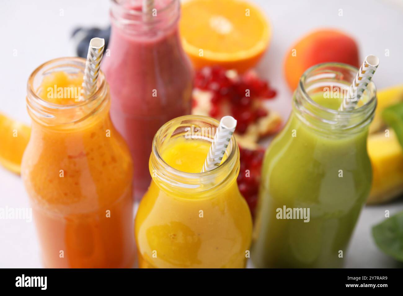 Glasflaschen mit leckeren Smoothies und verschiedenen Produkten auf weißem Tisch, Nahaufnahme Stockfoto