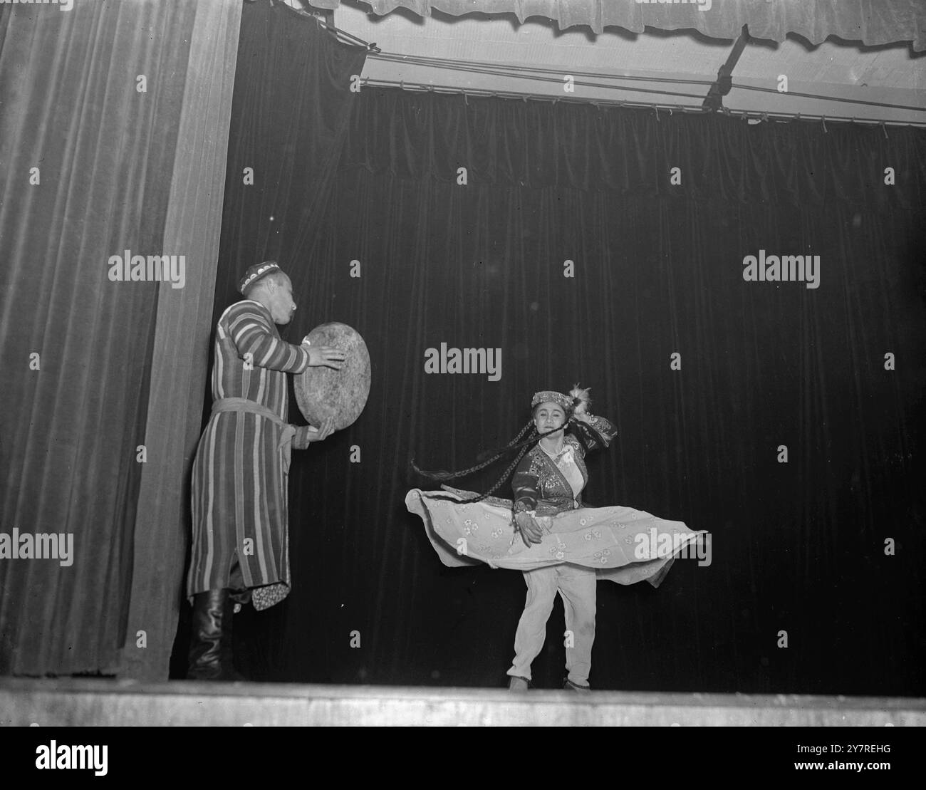 Usbekische Volkstänze in Walthamstow 5,1.54. Zwölf russische Studenten des Moskauer Konservatoriums kamen heute Morgen nach vielen Verzögerungen hierher. Sie sind die Gäste der Nationalen Studentenunion und haben heute Nachmittag auf dem von der Union organisierten Festival mit Musik und Tanz gespielt. Das Festival fand am South West Essex Technical College in Walthamstow statt. INP Fotoshows: Miss Gulnar Maveyeva führt einen exotischen usbekischen Volkstanz auf, während ein anderes Mitglied der Gruppe den Rhythmus auf einer Art Tambourin schlägt. Bild von Jack Davies. TDH/73634 International News Photos. Stockfoto