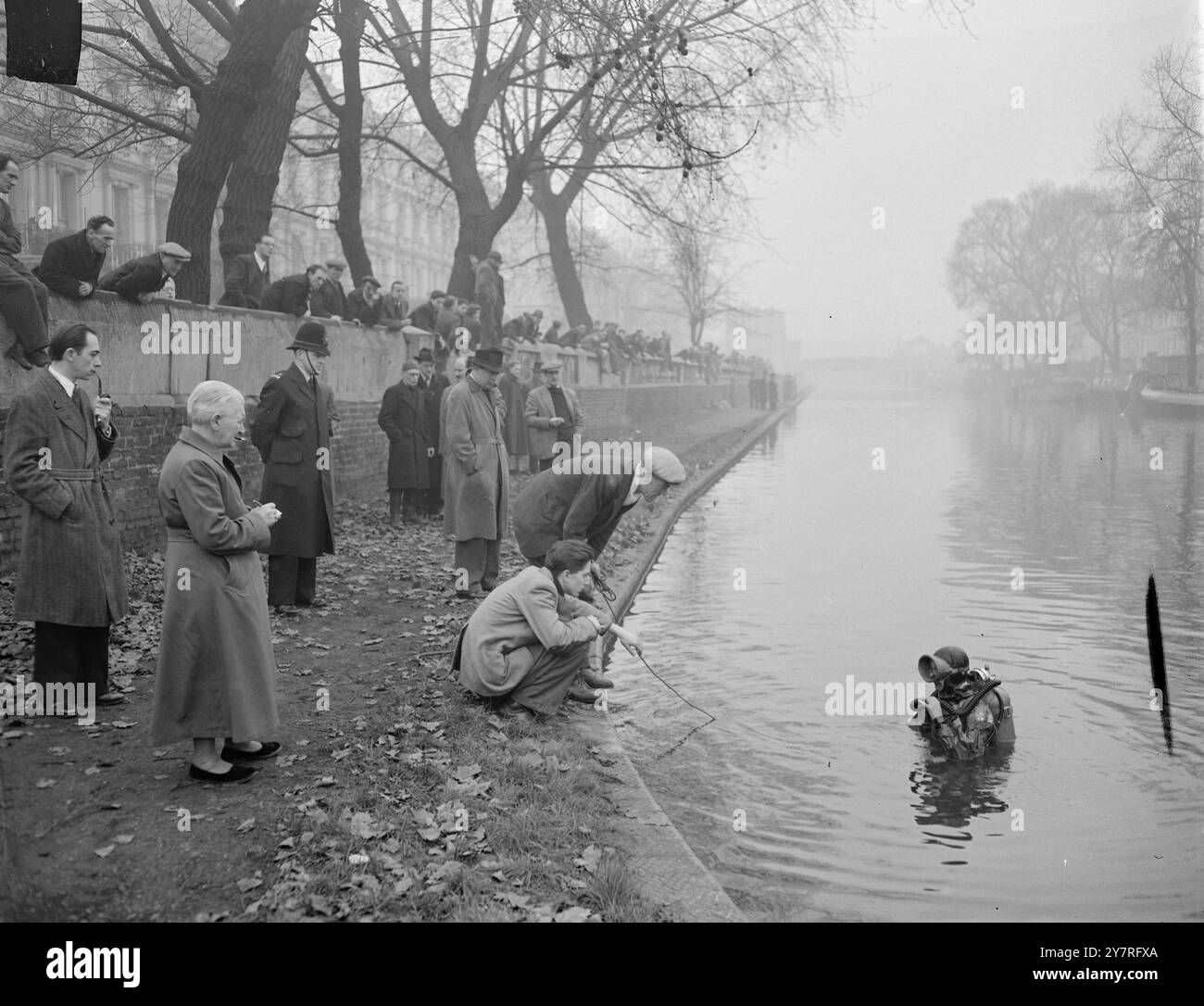 Frogwoman schließt sich der Kanalsuche nach dem vermissten Jungen an. Am 7.12.53 schloss sich die 23-jährige Sylvia Gregg heute Morgen der Suche nach der Leiche des sechsjährigen Teddy Willingdale an, der vermutlich im Grand Union Canal in Paddington ertrunken ist. Sie borgte sich einen Gummianzug mit Helm und Froschflossen vom Unterwasserzentrum in Dartford, dessen Cheflehrer Mr. Bram Martin, 35, seit gestern im Kanal durchsucht. I.N.P. Foto zeigt, dass Sylvia Gregg am Ende einer ihrer Recherchen heute Morgen eingesehen wird. Auf dem Schleppweg befindet sich der Großvater des vermissten Jungen (Hintergrund, links vom Polizisten Stockfoto