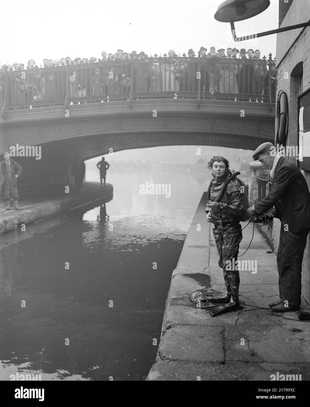 Frogwoman schließt sich der Kanalsuche nach dem vermissten Jungen an. 7.12.53. Die 23-jährige Sylvia Gregg hat sich heute Morgen der Suche nach der Leiche des sechsjährigen Teddy Willingdale angeschlossen, der vermutlich im Grand Union Canal in Paddington ertrunken ist. Sie borgte sich einen Gummianzug mit Helm und Froschflossen vom Unterwasserzentrum Dartford, dessen Cheflehrer Mr. Bram Martin, 35, er sucht seit gestern im Kanal. I.N.P. Foto zeigt nach einer dreiviertelstündigen Unterwassersuche lässt Sylvia Gregg ihre Ausrüstung für eine Pause auf dem Schleppweg entfernen. Bild von Jack Davies. S. 73137. Internat Stockfoto