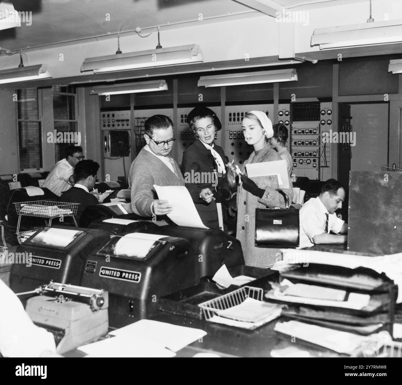 Miss World in den Nachrichten - kürzlich zur Miss World gewählt, Miss Finland, Marita Lindhahl, 18, besuchte den Nachrichtenraum von United Press International in der Fleet Street, London. Um herauszufinden, wie die Nachricht, dass sie den Titel Miss World gewann, so schnell zu ihr nach Hause kam, und hier, wie ein Fernschreiber die Nachrichten aus aller Welt sendet und empfängt, ist Henry Keyes vom europäischen Schreibtisch über einen Dolmetscher - 17. Oktober 1957 Stockfoto