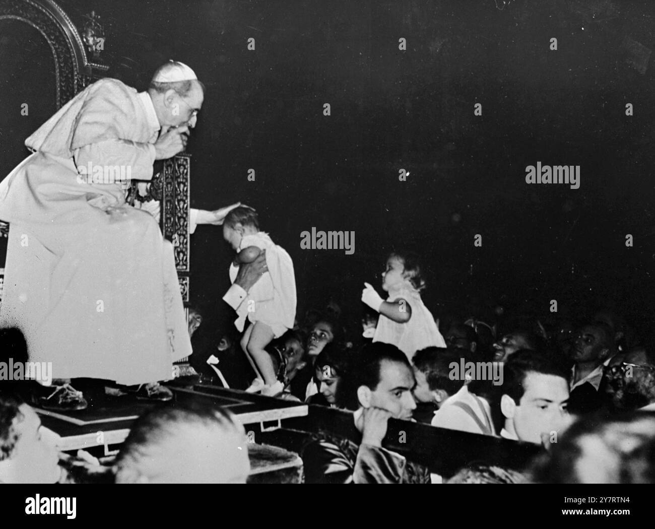 DER PAPST SEGNET KINDER viele Kinder waren in der großen Menge von Pilgern, die der Papst diese Woche in der Audienz des Petersdoms empfangen hat, bevor er Rom zu seinem Sommerpalast nach Castelgandolfo verlässt. Das Foto zeigt, wie Papst Pius XII. Den Kopf eines kleinen Kindes berührt, das aus der Menge zu ihm hochgehoben wurde. 15. Juli 1953 Stockfoto