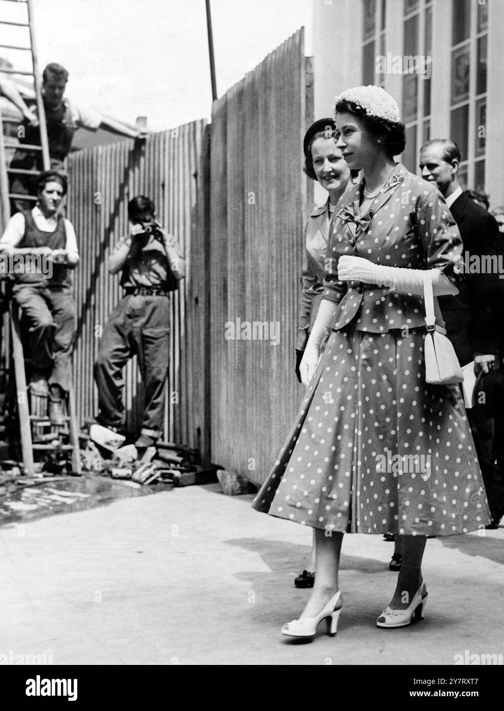 Die Königin in der Bildarbeit des Arbeiters kommt vorübergehend zum Stillstand, als die Königin vorbeikommt - und ein Arbeiter hebt seine Kamera, um ein Foto nach einem Krönungsgeheasal in Westminster Abbey in London zu machen. Der Königin, die ein graues Taffeta-Kleid mit Taubenmuster und weißem Seidenhut trägt, folgt am 26. Mai 1953 der Duke of Edinburgh Stockfoto