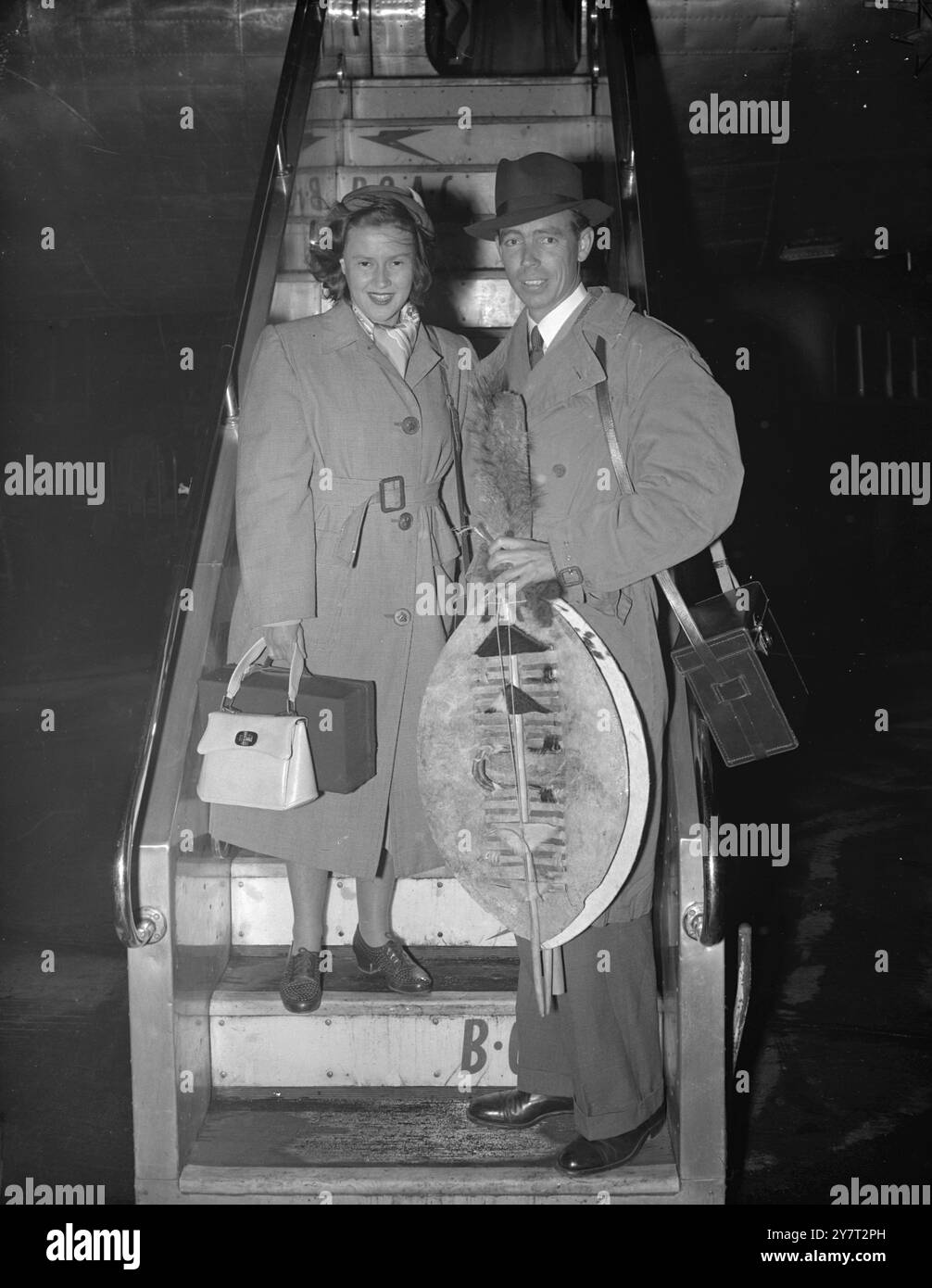 PIDDINGTONS SIND ZURÜCK - MIT SOUVENIRS VON ZUZULAND Mr. Sydney Piddington und seiner Frau Lesley - australische Gedankenleser-Partner, die einen Hit im britischen Radio gemacht haben -, die heute Abend von South African Airways Liner auf dem Londoner Flughafen gezeigt wurden. Mr. Piddington trägt Zulu-Schilde, die ihm in Zululand als Andenken an ihre neunwöchige Reise durch Südafrika präsentiert wurden. Die Pittington's werden einen Urlaub in London machen, bevor sie am 17. Dezember zu einer sechzehnwöchigen Australien-Tour aufbrechen. 29. November 1950 Stockfoto