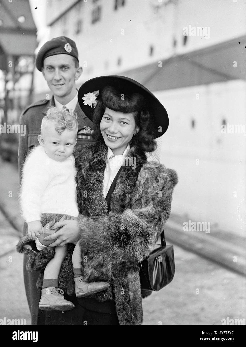 ZUHAUSE MIT SEINER BRAUT AUS HONGKONG, die einen ersten Blick auf Großbritannien in Southampton wirft, sind die Ehefrau und das elfmonatige Baby des Piloten II John Bartrum, R.A.F. aus Bembridge, Isle of Wight. Die Familie war Passagiere des Empire Trooper, der aus Fernost angekommen war. Frau Bartrum und das in Swatow, China, geborene eurasische Mädchen war früher Stewardess bei Hong Kong Airways. Pilot II Bartrum traf seine Braut als Doreen Joan - bei der Hochzeit eines Piloten der RAF in Hongkong. 16. Oktober 1950 Stockfoto