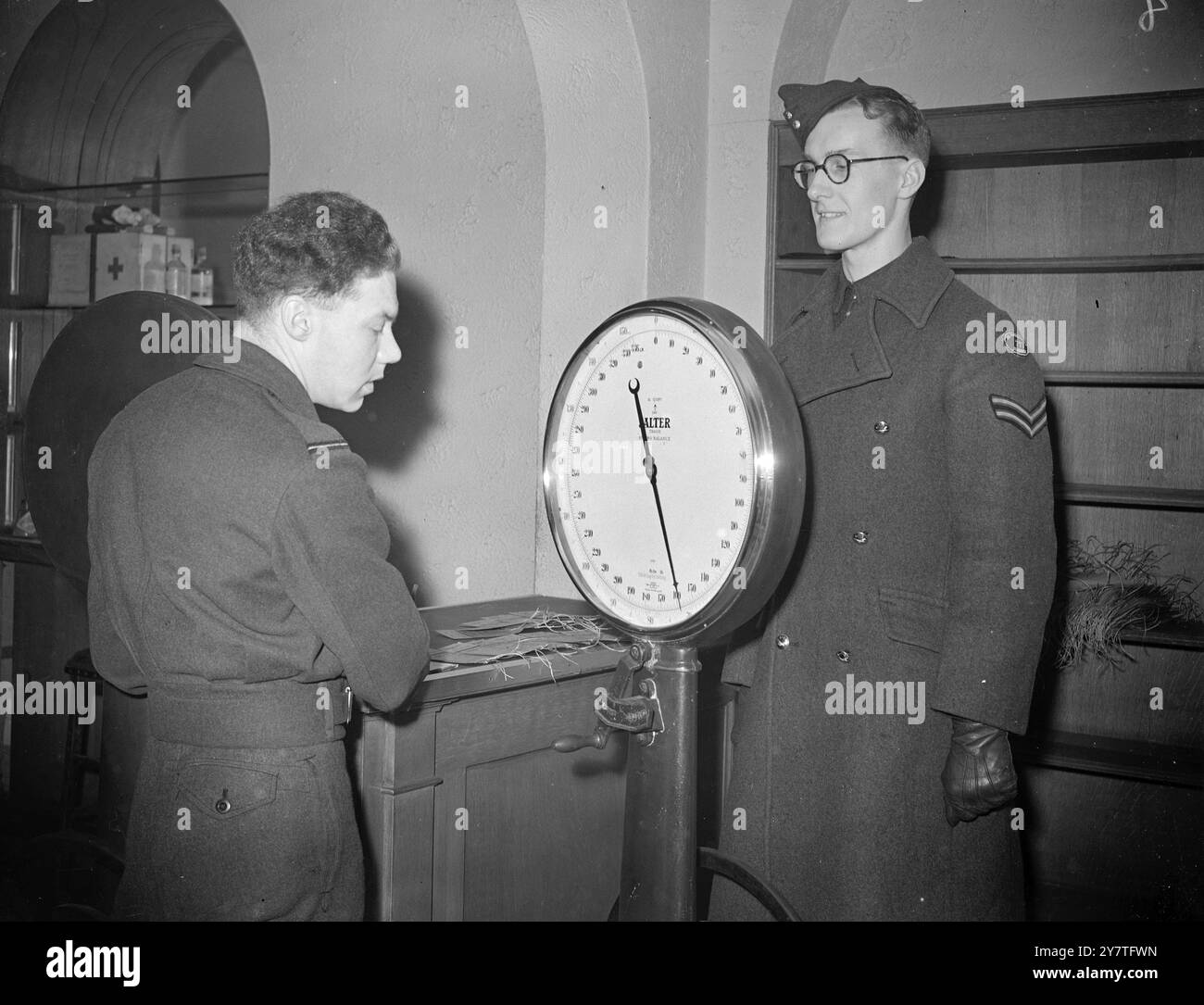 NACH SINGAPUR - FÜR 30 SCHILLING A.T.C.-CORPORAL PETER JOHN RALPH, 18 (rechts) von Cowes, Isle of White, auf der Waage stehend, während er im Air Booking Centre, Devonshire Street, London, eingewogen wird. Er wurde auserwählt, morgen an Bord der R. A. zu gehen A F-Flugzeug nach Singapur -- eines von 40 Kadetten der A.T.C. die jeden Monat als stellvertretende Luftquartiermeister auf Linienflügen der Transport Command nach Europa , in den Nahen Osten und in den Fernen Osten reisen . Alle Kadetten werden mit Kits geliefert, und die einzige Gebühr ist eine nominale Gebühr für -30 Schilling für Corporal Ralph's Singapur Stockfoto