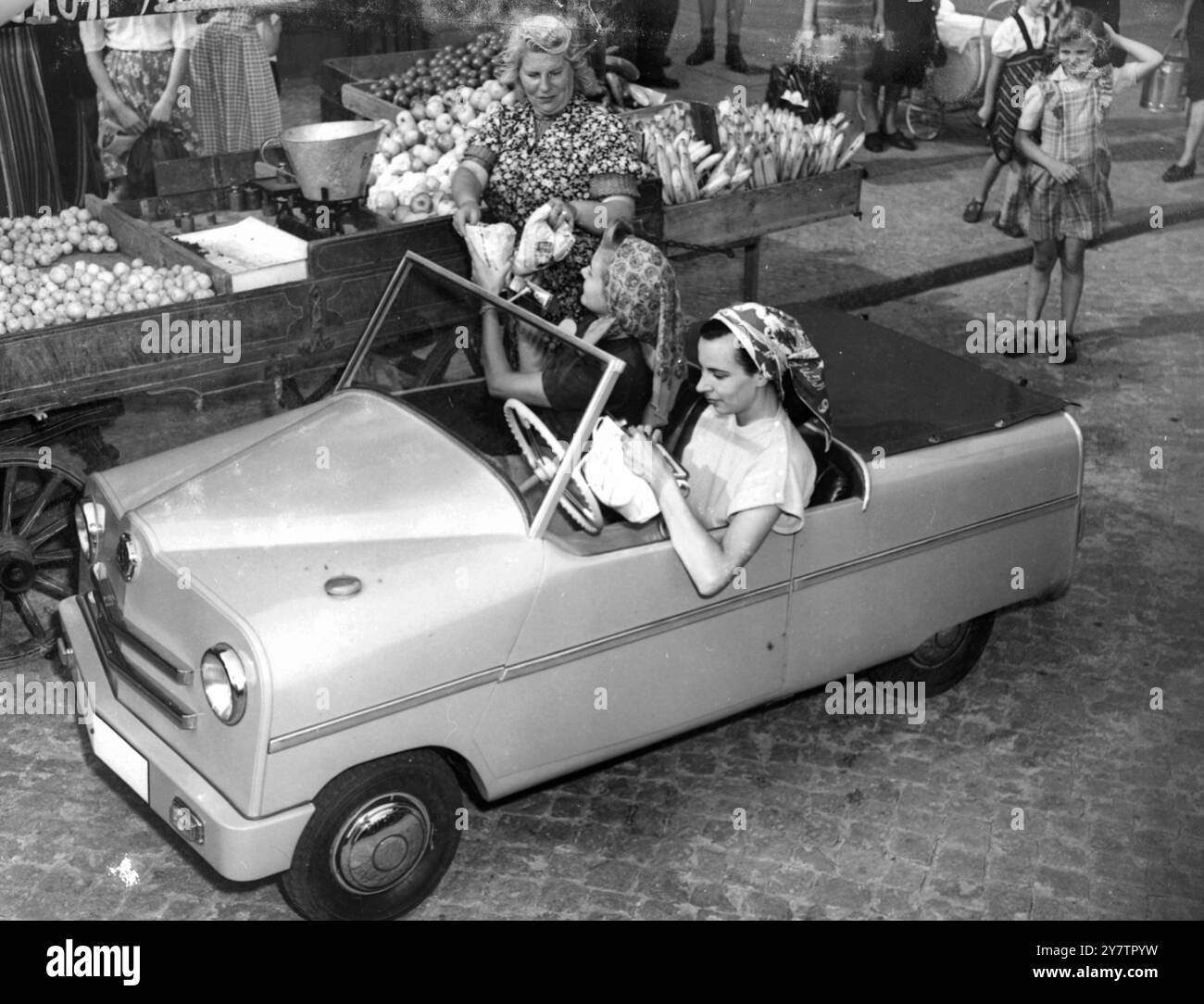 BERLINS 'SHOPPING-CAR' (UND ES SCHEINT, DASS DIE HAUSFRAU EINEN BRAUCHT!) - Zwei Berliner Hausfrauen testen ihren Einkaufswagen, entworfen von Helmut Butenuth. - Das intelligente Modell hat einen 6,2-PS-Motor am Heck, der eine Höchstgeschwindigkeit von etwa 45 km/h ermöglicht, und der Verbrauch beträgt etwa 80 km/l. Er wiegt 540 Pfund. (Beachten Sie den gut gestapelten Obststand im Hintergrund. Es scheint hier keinen Mangel an Bananen zu geben!) - 17. Juli 1950 Stockfoto