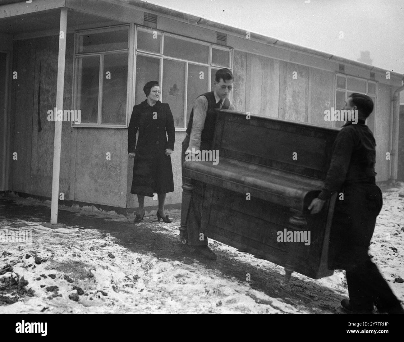 Das erste Fertighaus von Sandys wurde von Mrs. Mary Dyett, ihrem Ehemann und ihrer 17-jährigen Tochter Eileen, errichtet, seit Mr. Duncan Sandys Lord Portall übernahm. Bis sie in ihr neues Haus zogen , das eine von sechs vorgefertigten Wohnungen auf einem Bombengelände in der Thames Street, Greenwich, Südost-London ist, hatte die Familie Dyett, die aus ihrem eigenen Haus bombardiert wurde, in öffentlichen Notunterkünften geschlafen. Fotoshows: George Dyett und ein Freund tragen ein Klavier in das vorgefertigte Haus. Mrs. Dyett steht vor der Tür, George Stockfoto