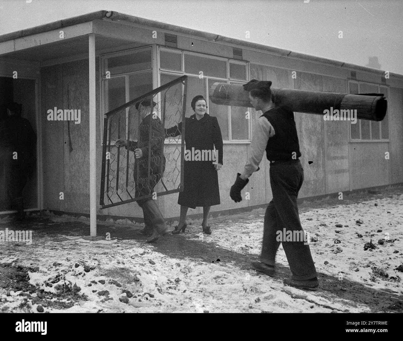 Das erste Fertighaus von Sandys wurde von Mrs. Mary Dyett, ihrem Ehemann und ihrer 17-jährigen Tochter Eileen, errichtet, seit Mr. Duncan Sandys Lord Portall übernahm. Bis sie in ihr neues Haus zogen , das eine von sechs vorgefertigten Wohnungen auf einem Bombengelände in der Thames Street, Greenwich, Südost-London ist, hatte die Familie Dyett, die aus ihrem eigenen Haus bombardiert wurde, in öffentlichen Notunterkünften geschlafen. Fotoshows: George Dyett und ein Freund tragen Möbel in das vorgefertigte Haus. Mrs. Dyett und ihre Tochter Eileen sind Standin Stockfoto