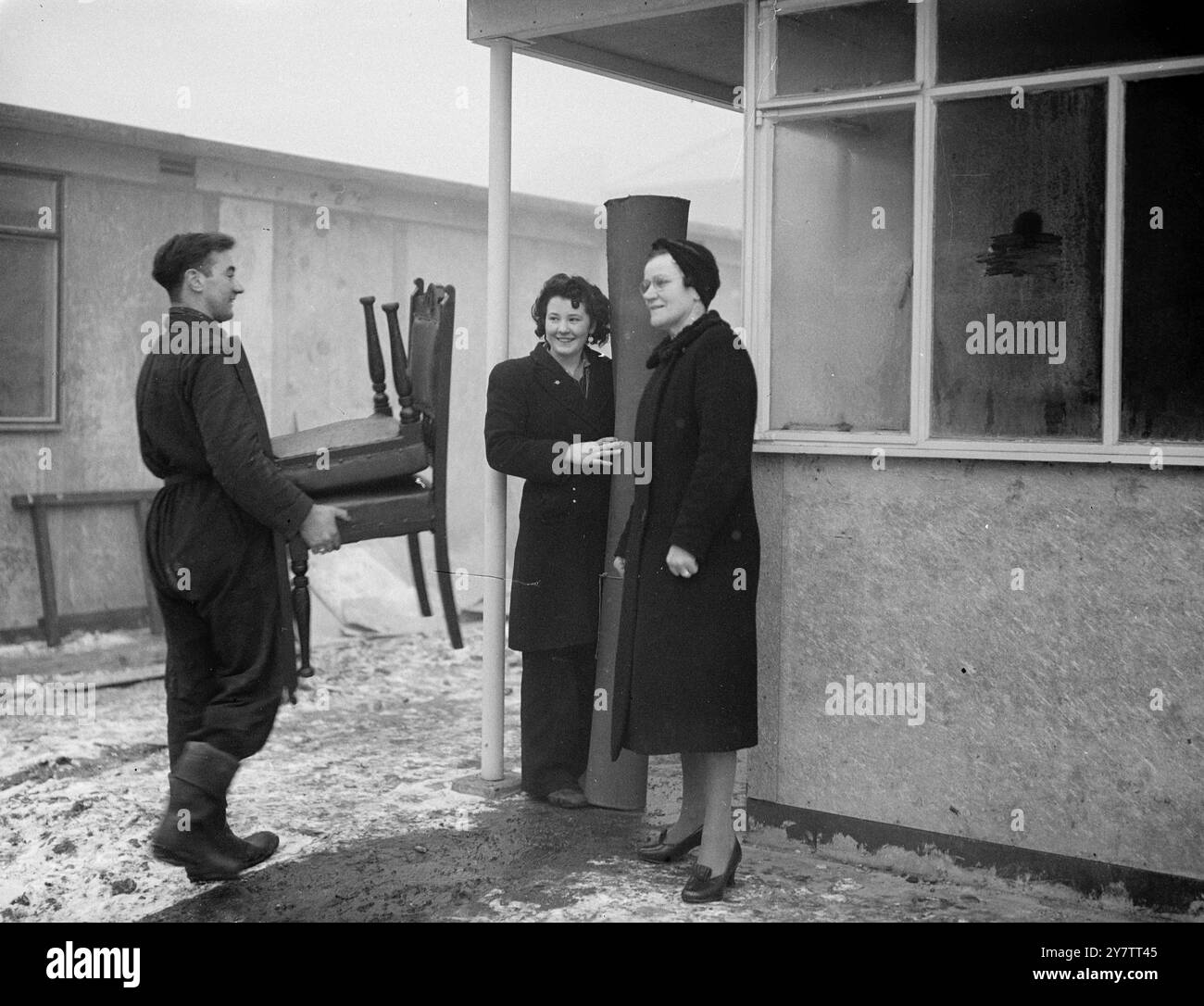 Das erste Fertighaus von Sandys wurde von Mrs. Mary Dyett, ihrem Ehemann und ihrer 17-jährigen Tochter Eileen bewohnt, seit Mr. Duncan Sandys Lord Portall übernahm. Bis sie in ihr neues Haus zogen , das eine von sechs vorgefertigten Wohnungen auf einem Bombengelände in der Thames Street, Greenwich, Südost-London ist, hatte die Familie Dyett, die aus ihrem eigenen Haus bombardiert wurde, in öffentlichen Notunterkünften geschlafen. George Dyett trägt Möbel in das vorgefertigte Haus. Mrs. Dyett und ihre Tochter Eileen stehen vor der Tür Stockfoto