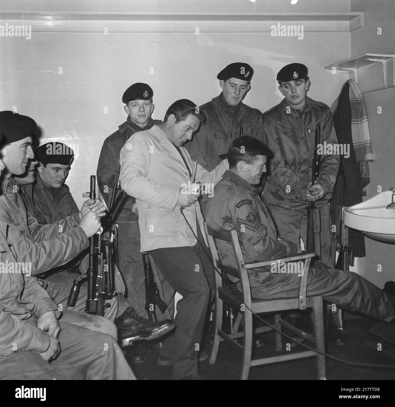 491152 'KÜRZERE HAARE FÜR WÄRMERE KLIMABEDINGUNGEN': FELIXSTOWE, SUFFOLK, ENGLAND: BUGLERS IN DER VORSTANDSPARTY DES 3. GRÜNEN JACKEN-REGIMENTS, DAS DERZEIT IN DER NORMANDIE STATIONIERT IST, SIND HEUTE HIER ZU SEHEN, DIE HAARSCHNITTE BEKOMMEN, UM AM FREITAG NACH HONGKONG ZU FLIEGEN, WO SIE GURKHAS FÜR DEN DIENST IN MALAYSIA ENTLASTEN WERDEN. UNSER BILD ZEIGT - HANDELNDE CPL. JOHN COOPER (22) VON ELM PARK, ROMFORD, ESSEX AUF DEM STUHL UND WIRD VOM FRISEUR HARRY HEDLEY, CIVILLAN FRISEUR VON FELIXSTOWE AUFGERÄUMT. COOPER, DER SEIT VIER JAHREN VERHEIRATET IST, HAT EINEN SOHN UND EINE TOCHTER. ICH SCHAUE VON LINKS NACH RECHTS Stockfoto