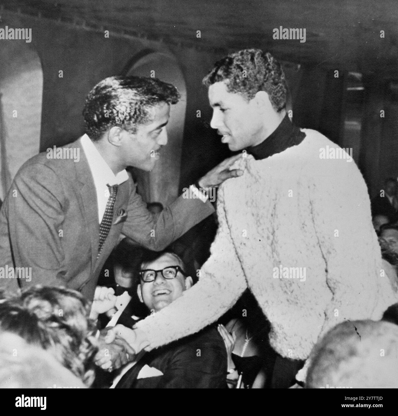 491051 "WO IST BILLY ECKSTINE?" NEW YORK, USA: EIN DUTZEND DER GRÖSSTEN NAMEN IM SHOWBUSINESS SORGTEN DAFÜR, DASS DIE SHOW GESTERN IN EINEM VERRÜCKTEN NEW YORKER NACHTLOKAL - DEM AMERICANA HOTEL - LIEF, ABER DAS LÄCHELN AUF DEN GESICHTERN VERDECKTE GROSSE SORGE UM DEN STAR, DER .... NICHT AUFTAUCHTE SÄNGER BILLY ECKSTINE. DER STAR SAMMY DAVIS JNR (LINKS), DER DEN VERMISSTEN KÜNSTLER ERSETZTE, SCHÜTTELT JEDOCH DIE HAND MIT ECKSTINES SOLDATENSOHN. KEN (21), DER IN NEW YORK ANGEKOMMEN WAR, UM DIE ERÖFFNUNG SEINES VATERS ZU SEHEN. KEN SAGTE, DASS SEIN VATER KRANK SEIN KÖNNTE. „ER HAT EINEN VIRUS IN AUSTRALIEN AUFGENOMMEN“, SAGTE ER, BILLY ECKSTINE SEI MIS GEWESEN Stockfoto