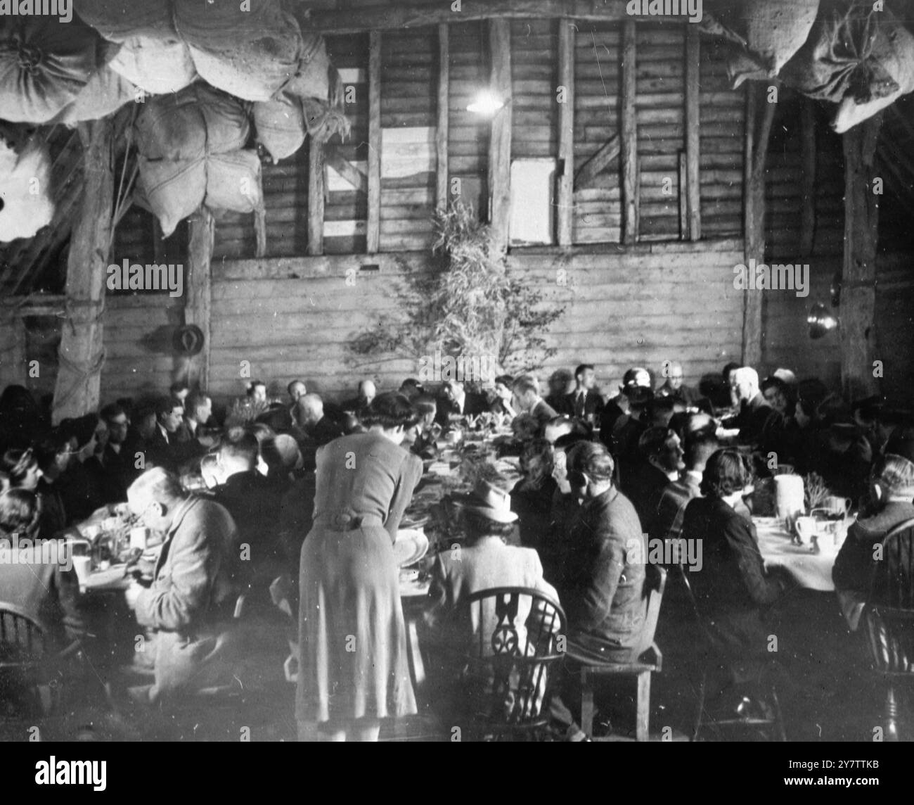 Ein Bauer aus Suffolk feiert mit hundert Nachbarn in seiner 400 Jahre alten Scheune das traditionelle Erntehaus. Vor zwei Jahren betrug der Ertrag 9 Ricks Mais und Heu, dieses Jahr sind es 19. Und das Geheimnis? „Wir versuchen hier etwas außer Lebensmitteln anzubauen“, sagt der Landwirt Peter Howard aus Lavenham. „Der Anbau von Mais ist zwar das Geschäft des Landwirts, aber der wachsende Charakter ist das Geschäft des Alltags. Nur so können wir die Ernte einer neuen Welt ernten. 1943 Stockfoto