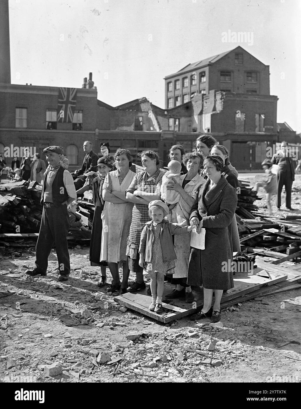 EAST LONDON FEIERT DEN ZWEITEN JAHRESTAG DER SCHLACHT UM GROSSBRITANNIEN anlässlich des zweiten Jahrestages der Schlacht um Großbritannien nahmen die Menschen von Stepney, einem sehr stark verwüsteten Gebiet im East End von London, an einem Gottesdienst Teil, den ihr Rektor, Reverend Reginald French, in den Ruinen einer geschossenen Schule im Bezirk durchgeführt hatte, um dem Mut der RAF-Männer zu gedenken, die London in der Schlacht um Großbritannien verteidigten. Frauen und Kinder hören sich den Gottesdienst an, der vor der geschädigten Schule in Stepney stattfindet. 15. September 1942 Stockfoto