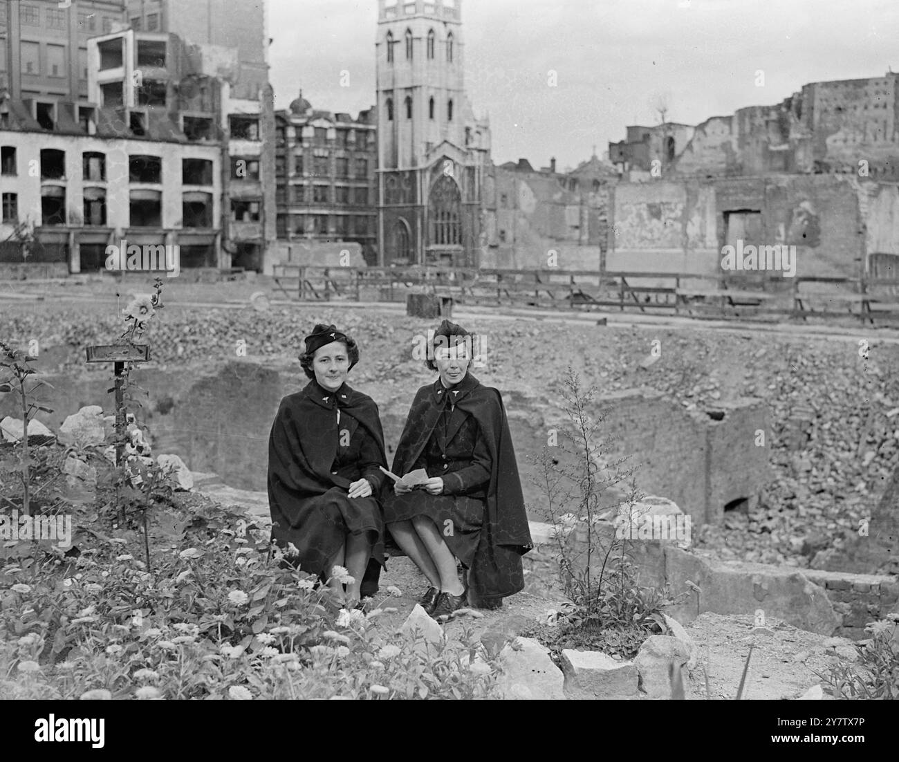 AMERIKANISCHE KRANKENSCHWESTERN SEHEN BOMBE BESCHÄDIGTE STADT Foto zeigt: Zwei amerikanische Krankenschwestern aus Kansas City, USA, heute in London, besuchten einige der bombardierten Gebiete der City of London. Hier werden sie zwischen den Trümmern von bombardierten Gebäuden sitzen gesehen, wo auch Blumen wachsen. Sie sind Second Lieutenant Marion Cross (links) und Second Lieutenant Dorothy Downs. 18. September 1942 Stockfoto