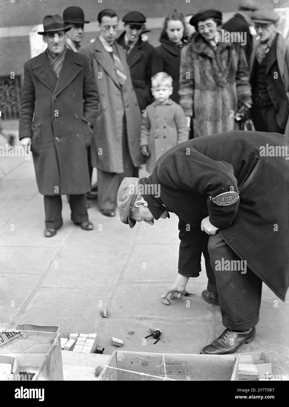 WARTIME LONDON STRASSENVERKÄUFER HABEN NUR HAUSGEMACHTE SPIELZEUGE -- Spielzeug, vor allem die billigeren Arten, die normalerweise von den Straßenhändlern verkauft werden, (oder Händlern), sind fast aus den Straßen von Wartime London verschwunden. Dieser lizenzierte Straßenhändler, der das von der Corporation of the City of London ausgegebene Armband trägt, hat nur einen kleinen Bestand an mechanischen Spielkästen zum Verkauf. - Dezember 1941 Stockfoto