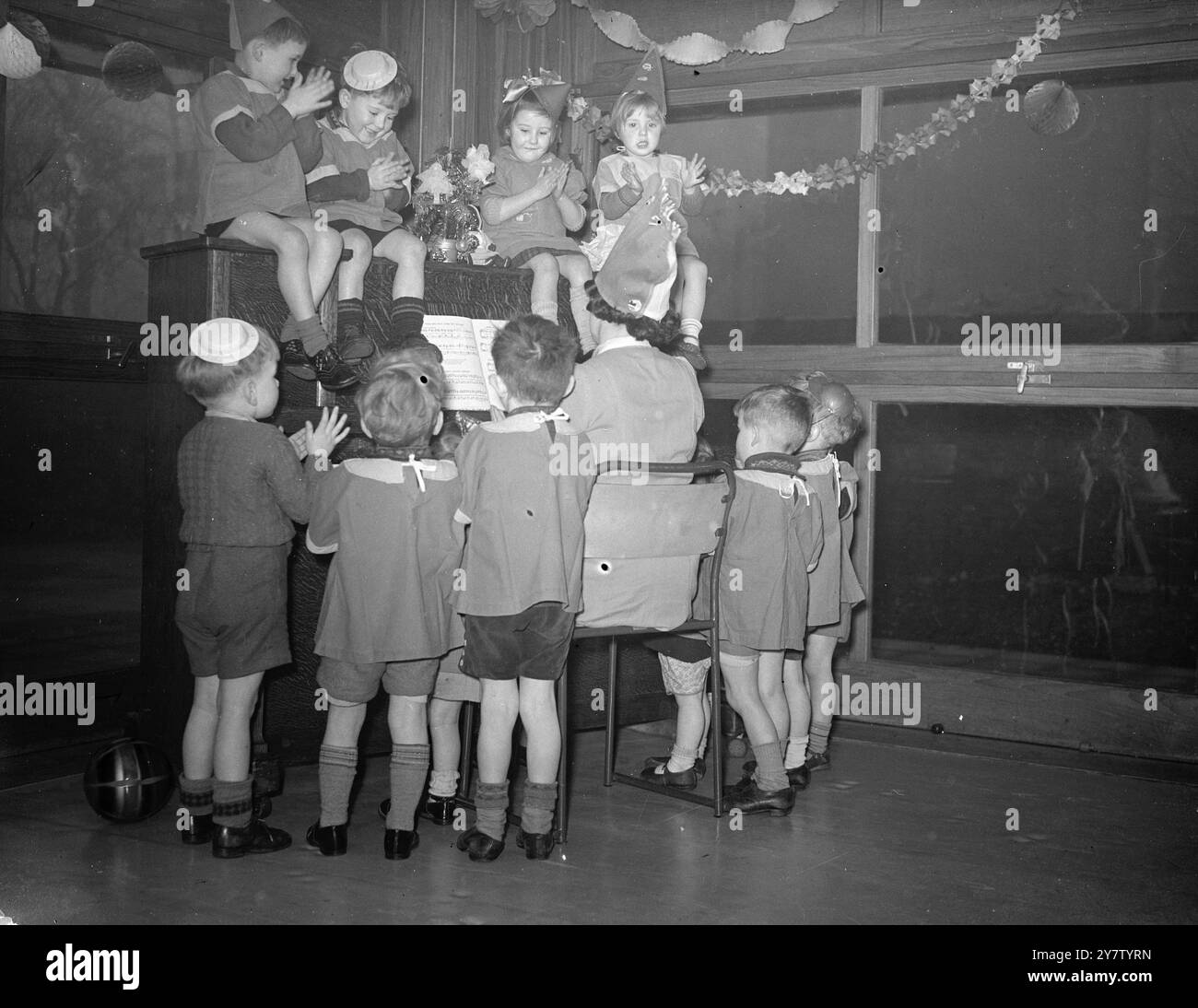 Eine WEIHNACHTSFEIER - TOTTENHAM DAY KINDERGARTEN Kinder in einem Day Kindergarten für Kinder unter fünf Jahren, deren Väter größtenteils in der Armee sind und deren Mütter arbeiten, haben trotzdem ein angenehmes Chirurgie erlebt. Foto zeigt: Die Kinder stehen um das Klavier und einige sitzen sogar auf dem Klavier und genießen ein Lied. 18. Dezember 1940 Stockfoto