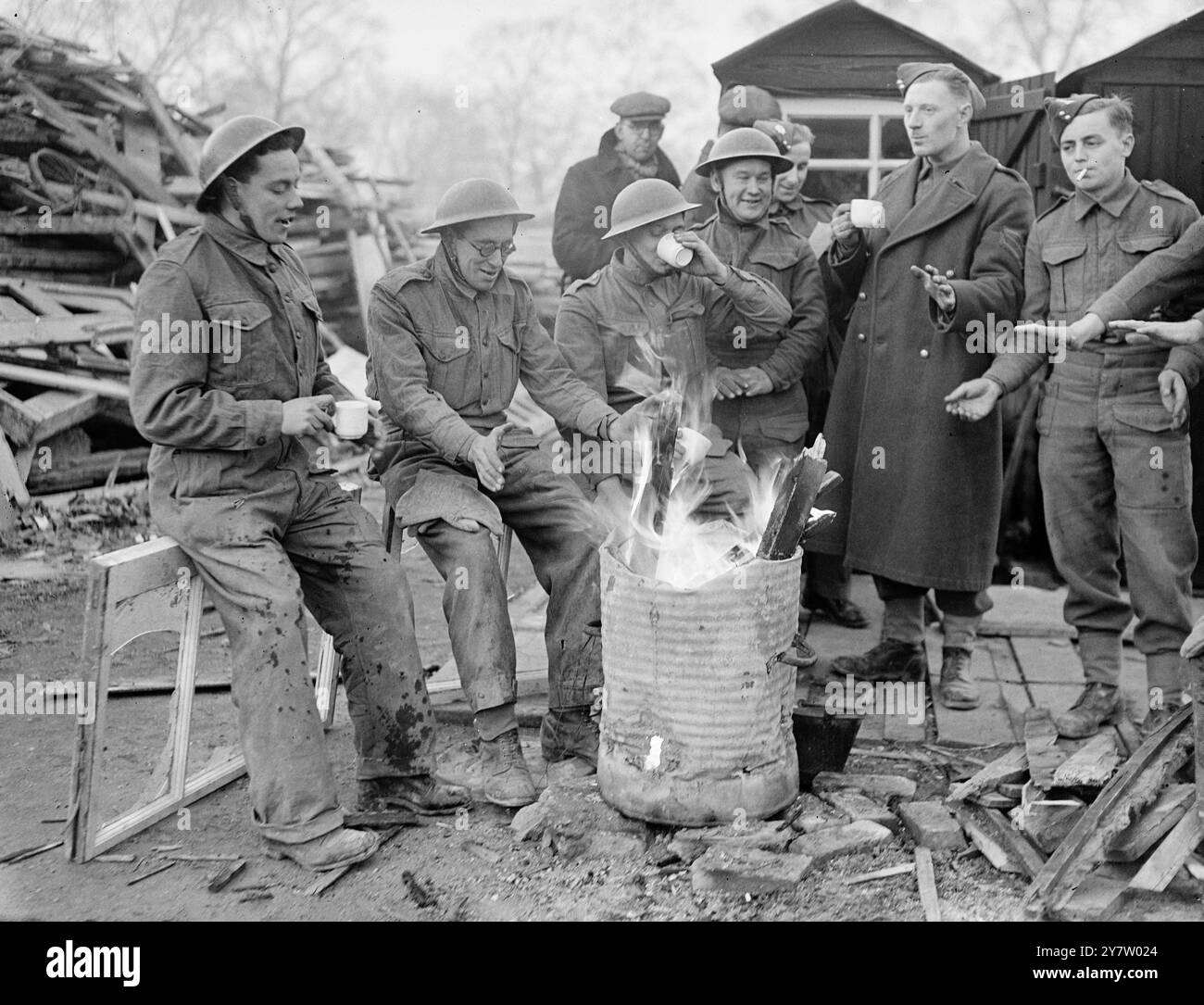 PIONIERE ERFRISCHEN SICH FÜR MEHR ARBEIT Foto zeigt: Männer des Pionierkorps sitzen um ein Feuer und genießen eine Tasse Tee während einer Pause in ihrer Arbeit. Diese Männer sind an der Bergung von Material aus beschädigten Gebäuden beteiligt. 9. Dezember 1940 Stockfoto