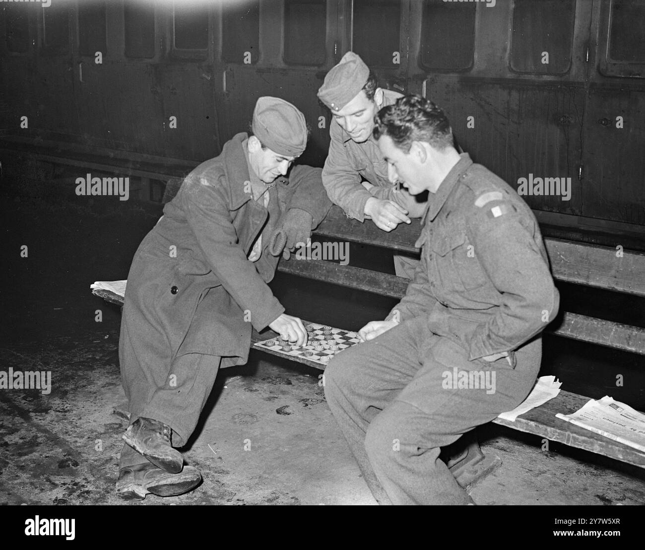 ITALIENISCHE KRIEGSGEFANGENE SPIELEN IN DER PADDINGTON STATION EIN SPIEL DER ZUGLUFT. Foto zeigt: Zwei italienische Kriegsgefangene, die Teil einer Zahl sind, die zur Unterstützung der Feiertagsstürme an Londoner Bahnhöfen eingezogen wurden, beschließen, sich mit einem Spiel der Zugluft niederzulassen, während ein dritter Kamerad auf der Paddington Station in London zusieht. 19. Dezember 1945 Stockfoto