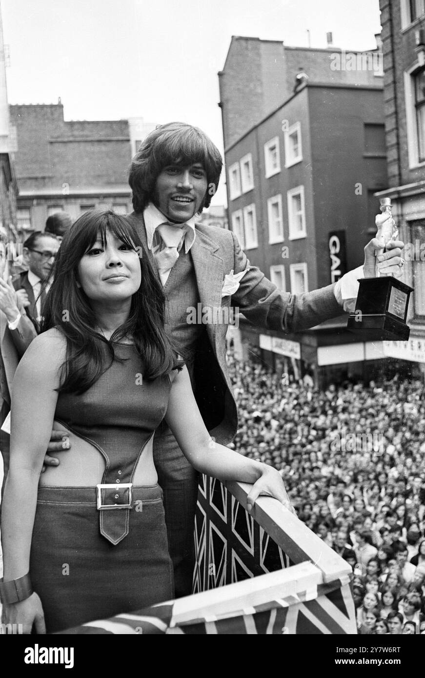 Über Hunderten von Popfans in der schicken Carnaby Street in London heute Nachmittag, hält Barry Gibb, der Anführer der Popgruppe Bee Gees, die Statuette im Wert von 500 Pfund hoch, die ihm von der Schauspielerin Tsai Chin für den Titel Großbritanniens am besten gekleideten Pop Star von Radio Luxembourg verliehen wurde. Die Präsentation auf dem Balkon von John Stephen's Boutique ist Teil eines „Youthquake“, das heute im „Mod“-Modezentrum in London, England stattfindet. Die Statuette in Silber ist eine geformte Figur von Beau Brummel. 12. Juli 1969 Stockfoto