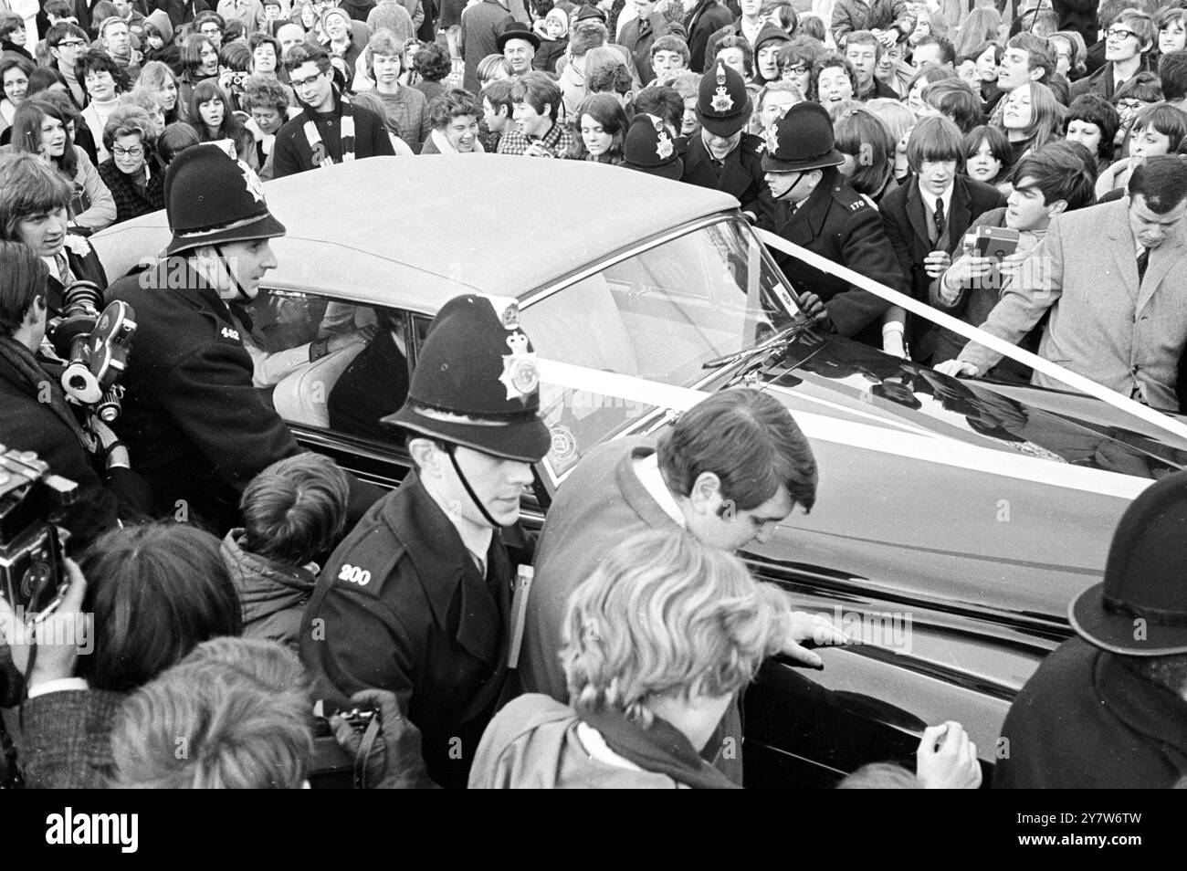 Die Polizei verbindet Waffen, um die Menge zurückzuhalten, als Sänger Lulu und Maurice Gibb von der Bee Gees-Gruppe nach ihrer Hochzeit in der St. James's Church, Gerrards Cross, Buckinghamshire, England, am .18. Februar 1969, abreisen Stockfoto