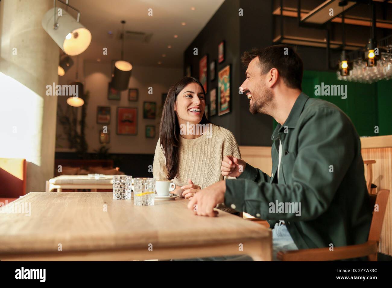 Zwei Freunde teilen sich Lachen und warme Drinks in einem charmanten Café und schaffen eine einladende Atmosphäre, die an einem sonnigen Tag die Verbindung und Freude feiert Stockfoto