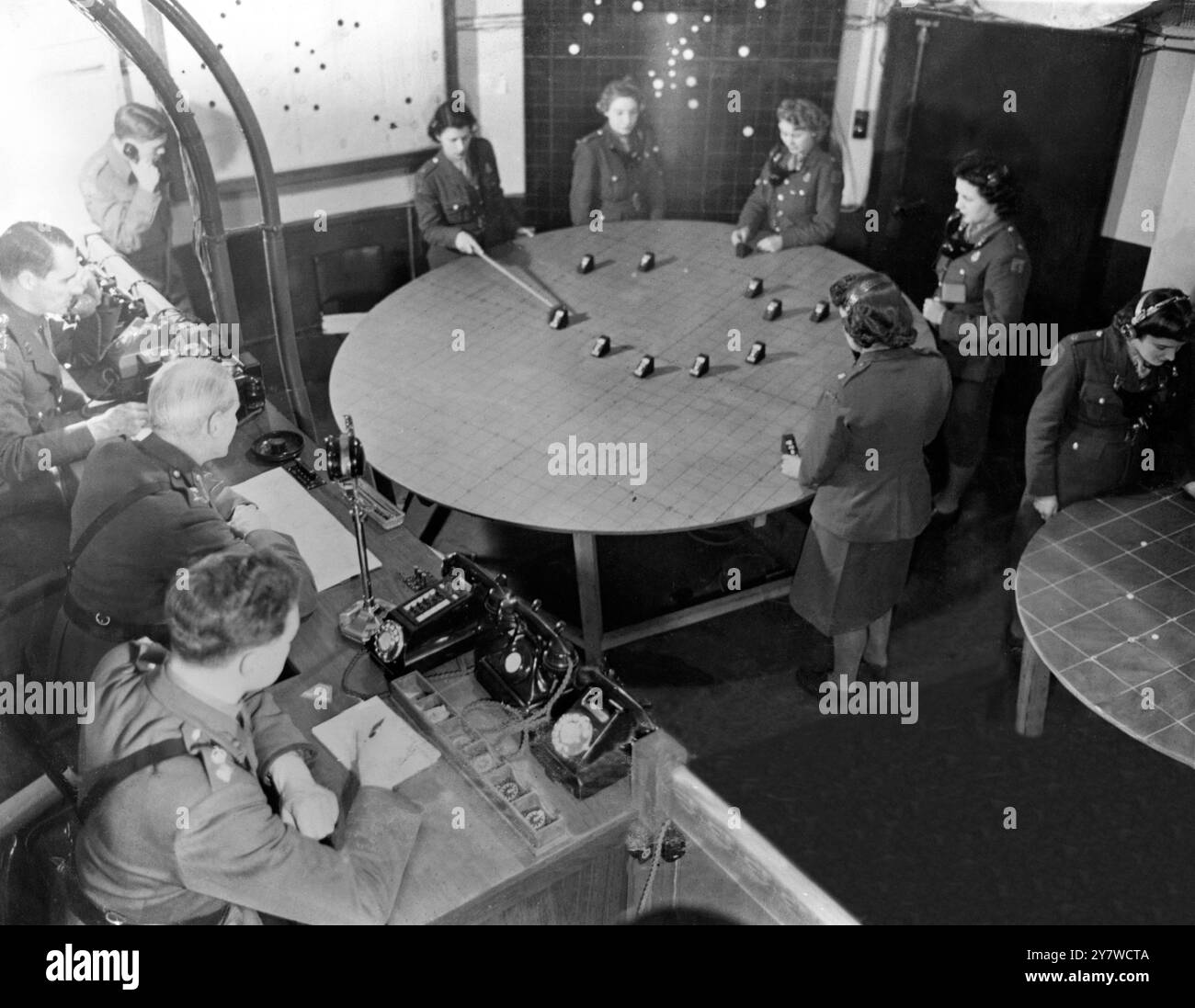 Londons A.A.-Barrage wird von einem hochrangigen Armeeoffizier kontrolliert, der auf einer Plattform im Waffenkontrollraum tief unter dem Boden sitzt. Durch ein Mikrofon gibt er Befehle an die Waffenstandorte. Er wird hier (Mitte) mit seinem Offizierspersonal gesehen, wie er die Verschwörung von Flugzeugflugzeugen bt ATS Mädchen im Kontrollraum beobachtet. Der Offizier, der der Kamera am nächsten ist, kontrolliert die Höhe des Feuers und die Art der zu verwendenden Muscheln mit Hilfe seiner farbigen Uhren. (2. Weltkrieg) 24. Juli 1944 Stockfoto