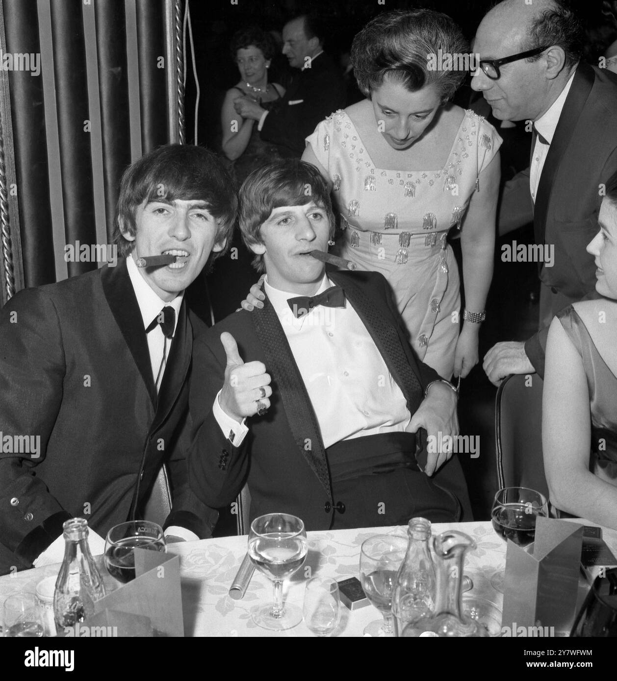 Beatles George Harrison (links) und Ringo Starr rauchen Zigarren bei einer Galavorstellung im Empire Ballroom am Leicester Square London - 24. März 1964 Stockfoto