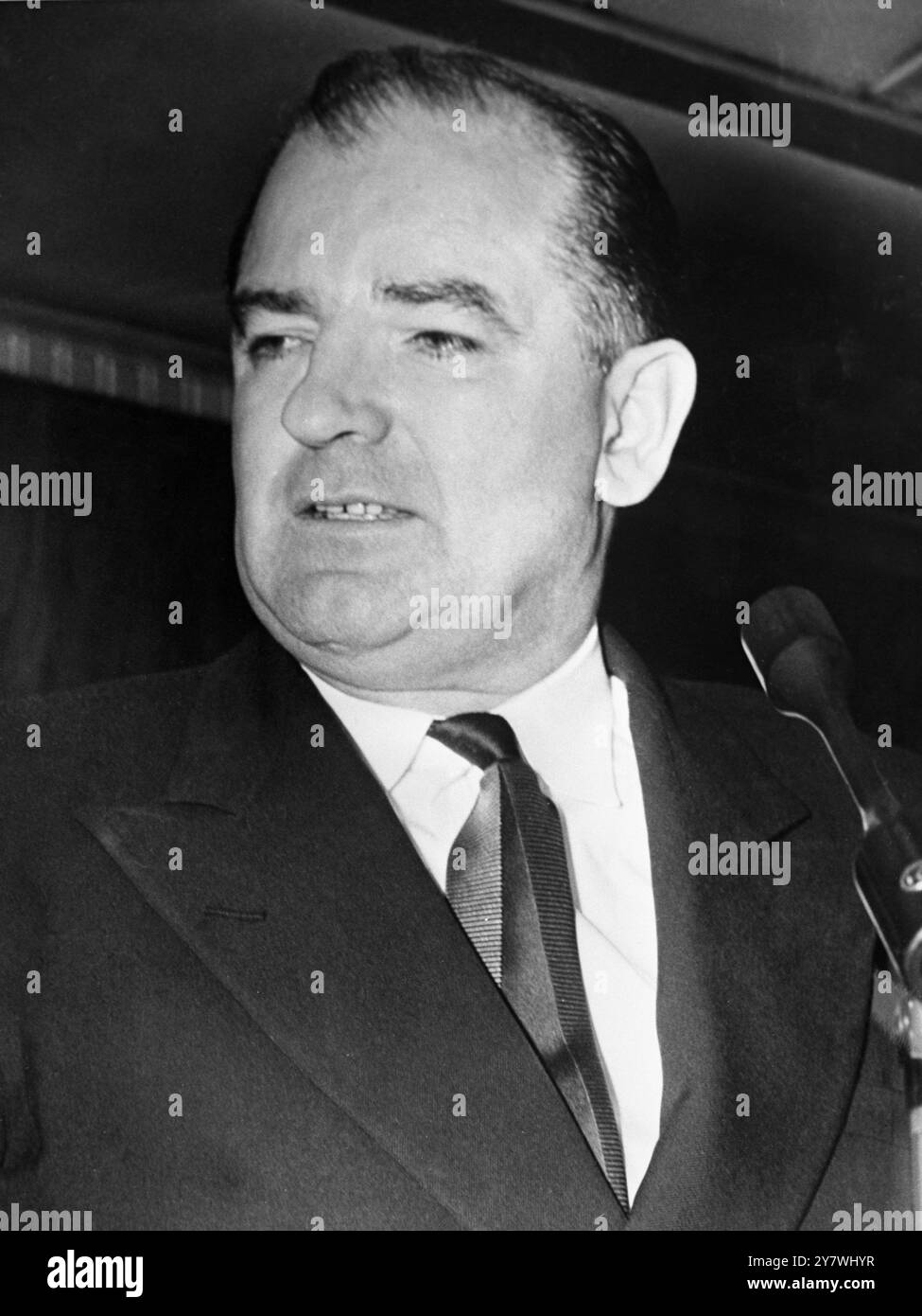 Senator Joseph McCarthy aus Wisconsin sieht düster aus, als er bei seiner Rückkehr nach Washington mit Nachrichtensprechern spricht. Vor dem Verlassen seines Heimatstaates sagte der Senator, er habe einen "geheimen Zeugen " , der seine Anklage untermauern kann , dass der Armeeminister Robert Stevens versucht habe , seine Untersuchung der Armee durch Anbieten von "Dreck" auf Marine und Luftwaffe abzuwenden . März 1954 Stockfoto