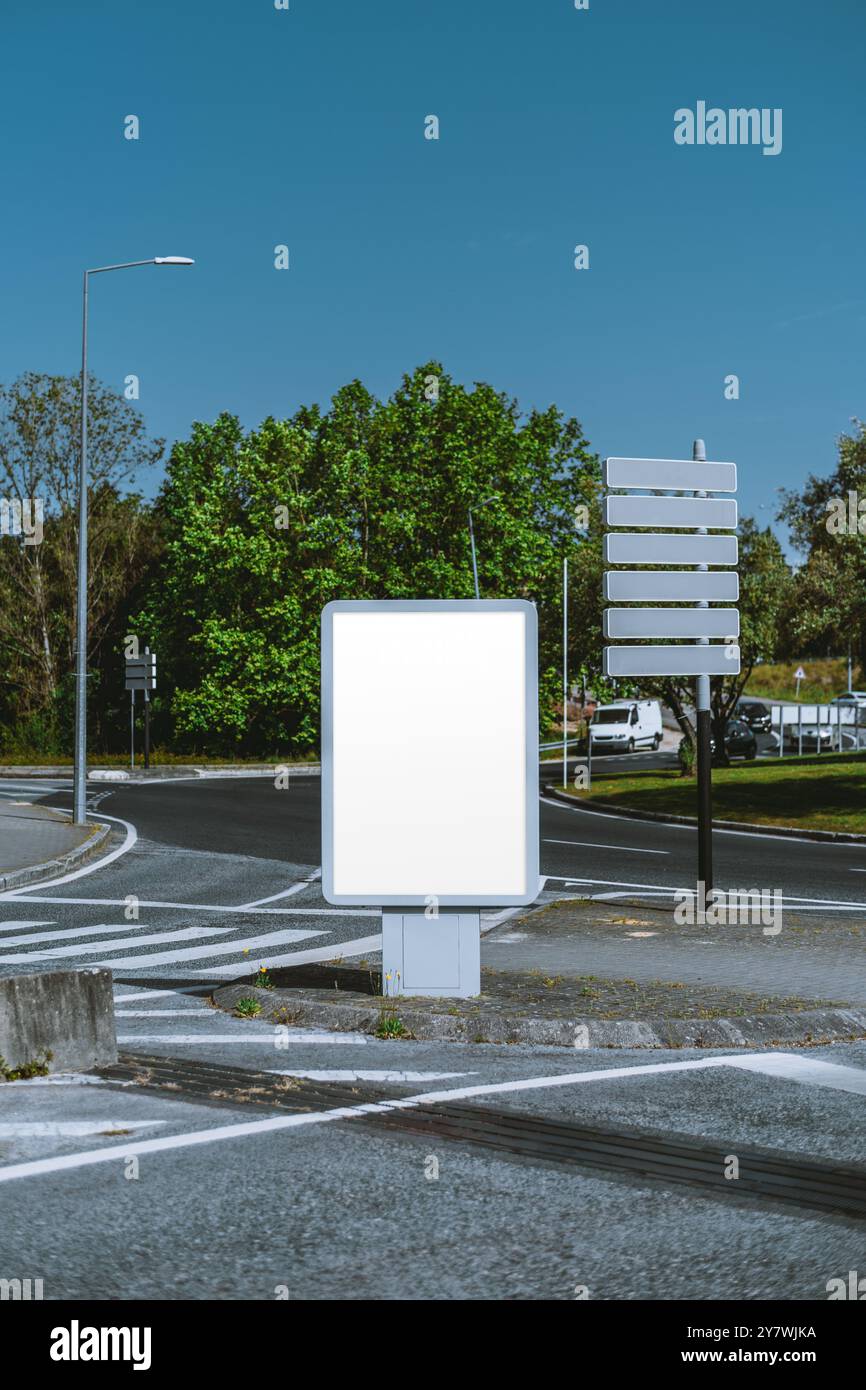 Vertikale Aufnahme eines Mockups einer leeren Plakatwand und leere Richtungsschilder an einem Kreisverkehr. Klarer Himmel, Grün und Straße sichtbar. Perfekt für Stockfoto