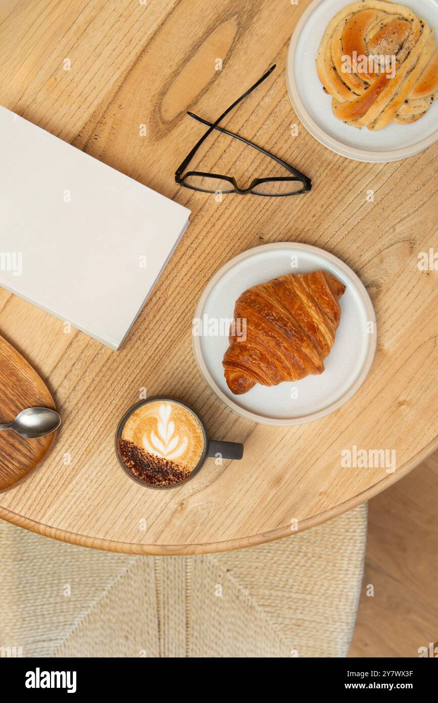 Ein Tisch in einem Café mit einer Tasse Cappuccino, köstlichem Gebäck und Zeitschriften. Draufsicht. Stockfoto