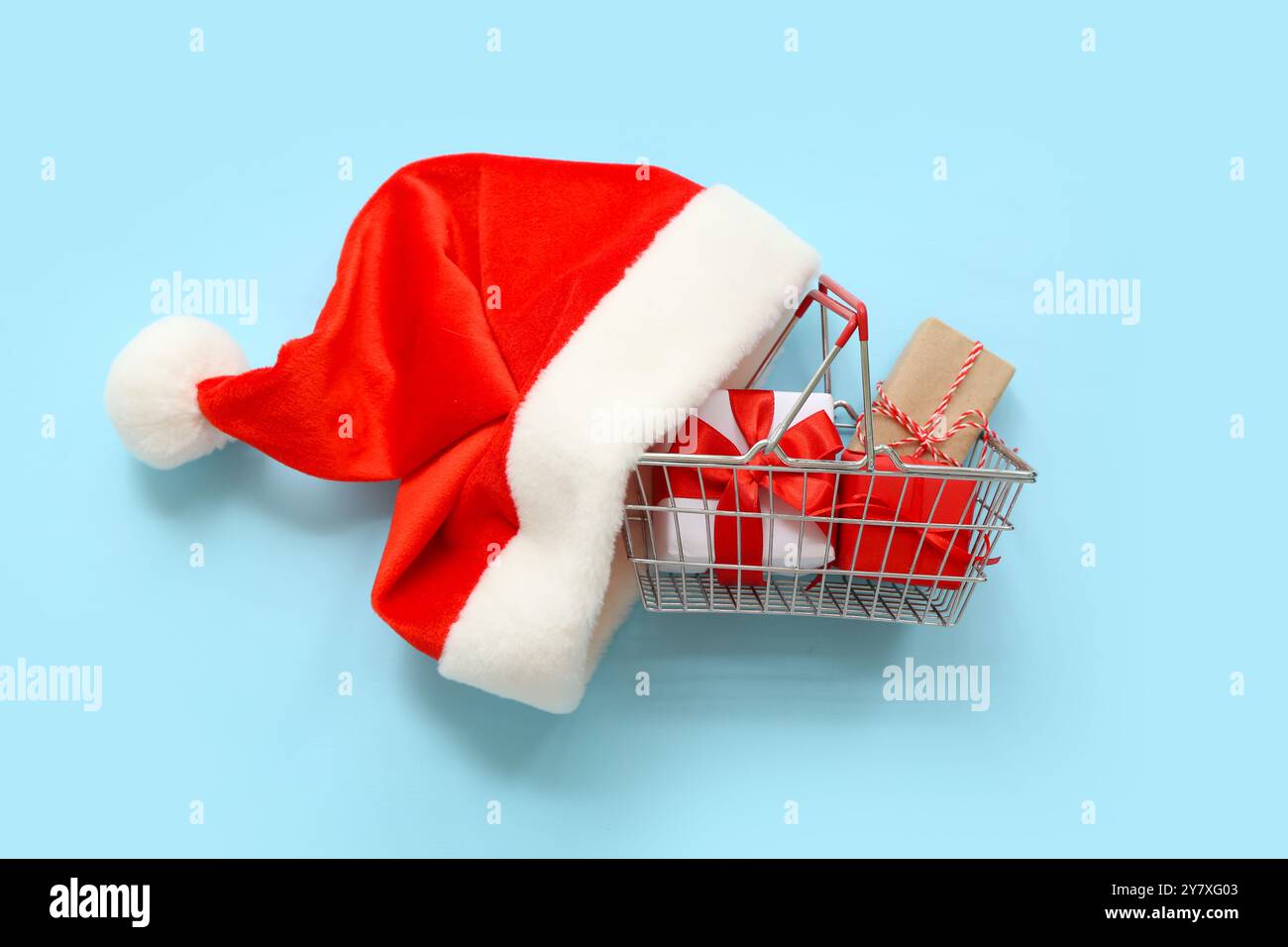 Mini-Einkaufskorb mit Weihnachtsgeschenken und Weihnachtsmann-Hut auf farbigem Hintergrund Stockfoto