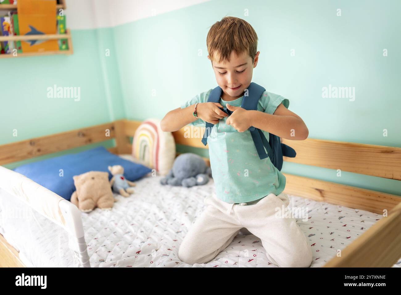 Der Junge kniete auf dem Bett und zog seinen Rucksack an, um zur Schule zu gehen Stockfoto