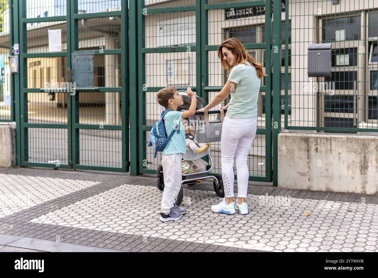 Junge High-Five und Abschied von seiner Mutter und dem kleinen kleinen Bruder am Schuleingang Stockfoto