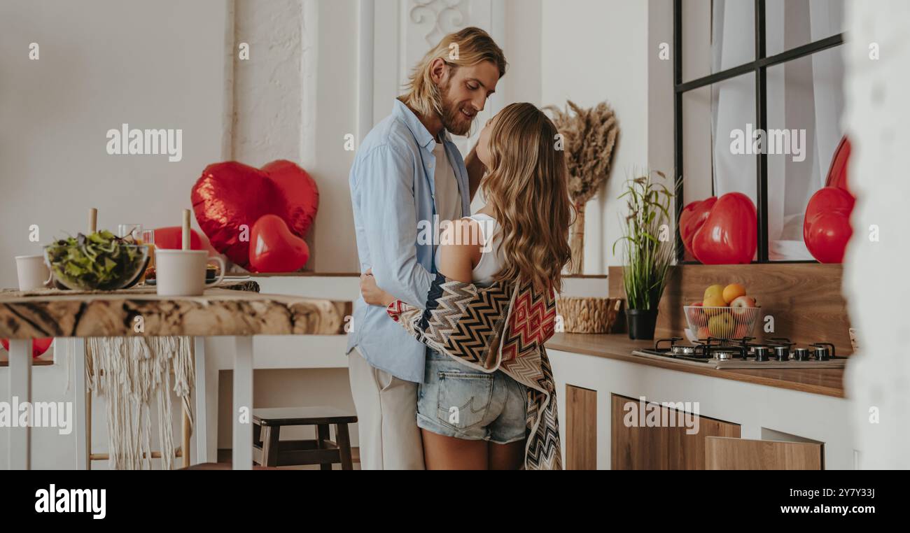 Romantisches junges Paar, das sich umschließt und küsst, während es den Liebesjubiläum in dem dekorierten Haus feiert Stockfoto