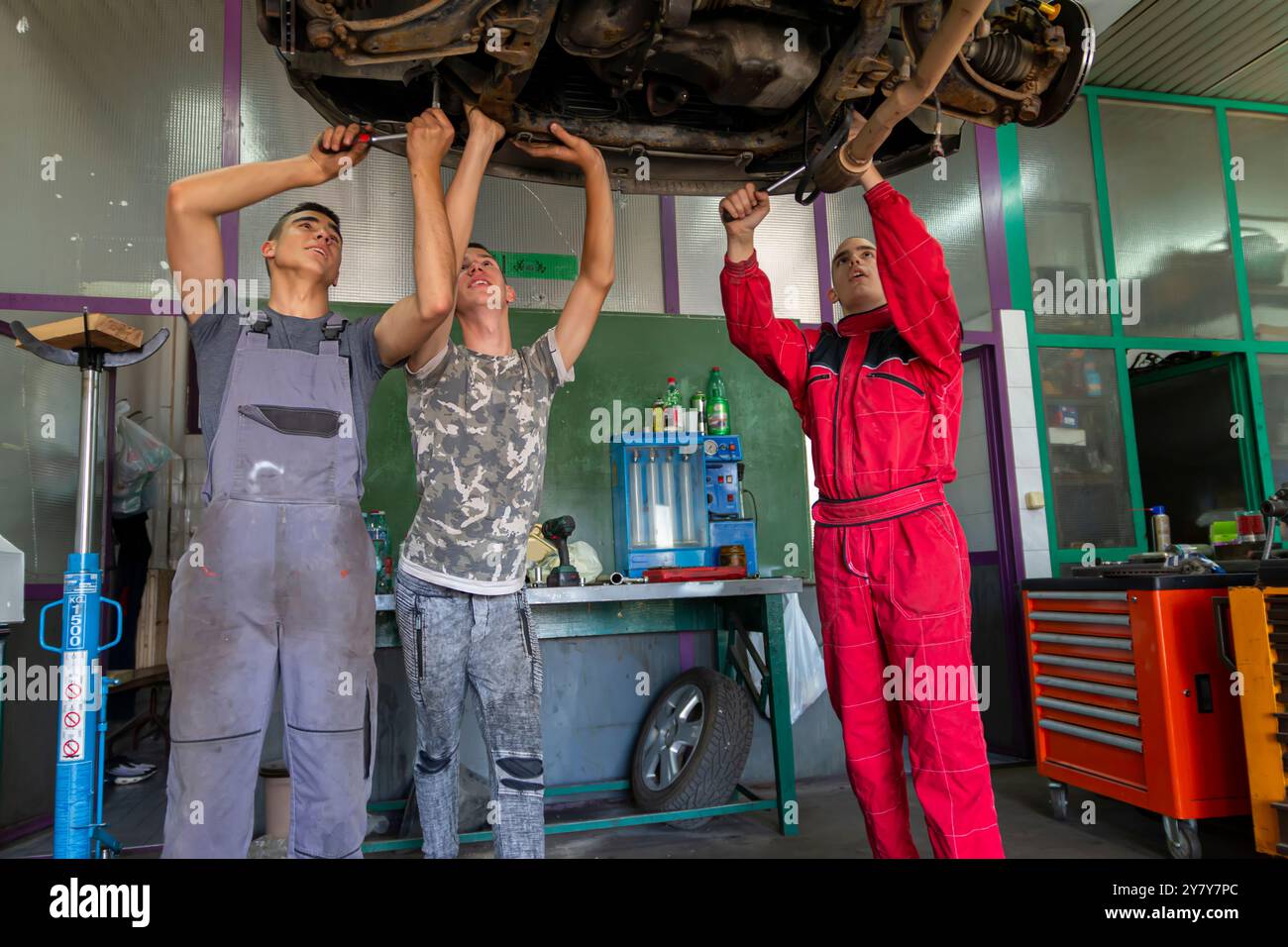 Junge Automechaniker unter dem Auto auf der hydraulischen Rampe bei der Arbeit in der Werkstatt Stockfoto