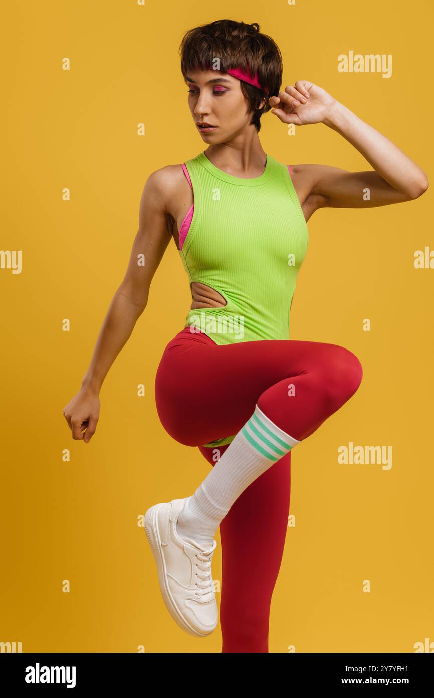 Selbstbewusste junge Frau in Sportbekleidung im Retro-Stil, die vor gelbem Hintergrund trainiert Stockfoto