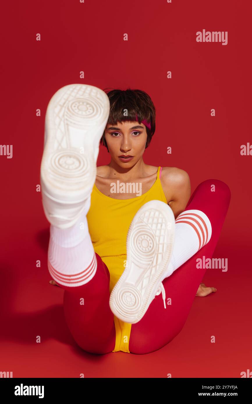 Selbstbewusste junge Frau in Sportbekleidung im Retro-Stil, die vor rotem Hintergrund trainiert Stockfoto