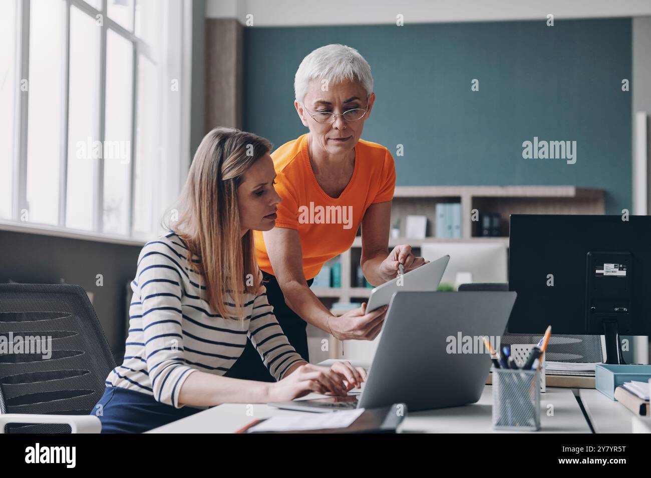 Zwei selbstbewusste Frauen diskutieren während sie gemeinsam im Büro arbeiten Stockfoto